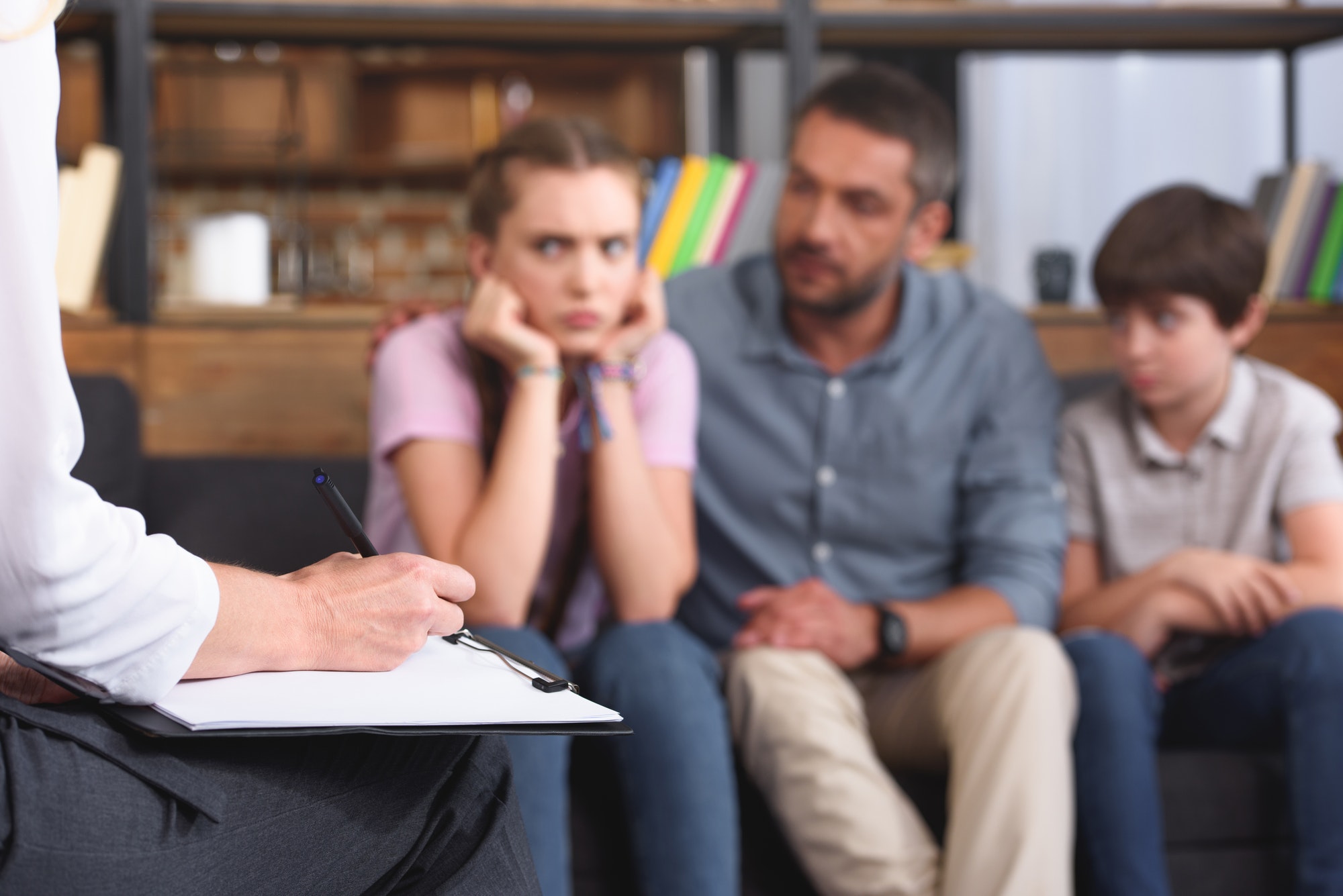 cropped image of female counselor writing in clipboard while family sitting on sofa on therapy