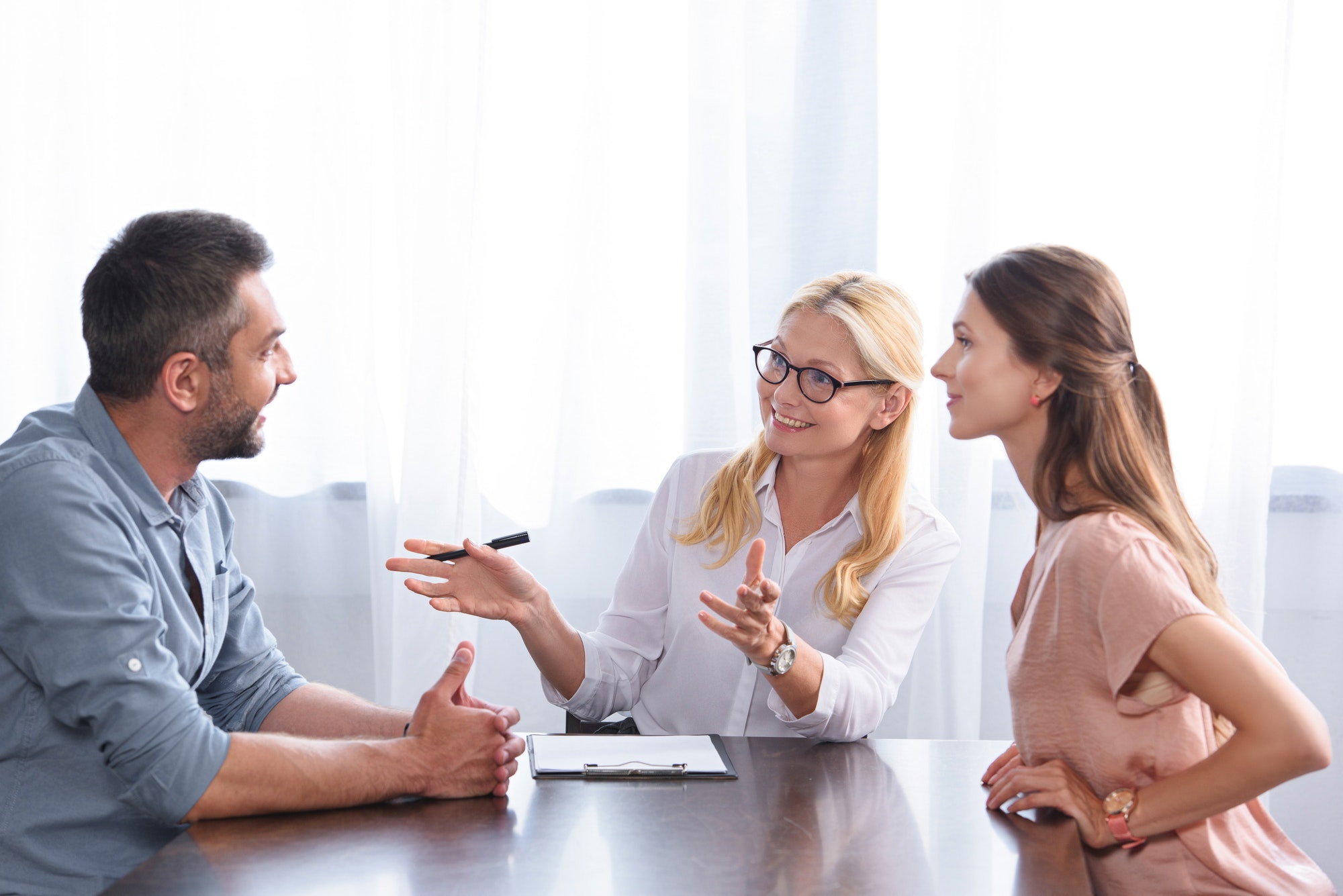 smiling female counselor gesturing by hands and talking to couple on therapy session in office